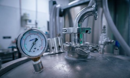 Close-up of a pressure gauge on a stainless steel tank in a sterile industrial setting, showcasing manufacturing technology.